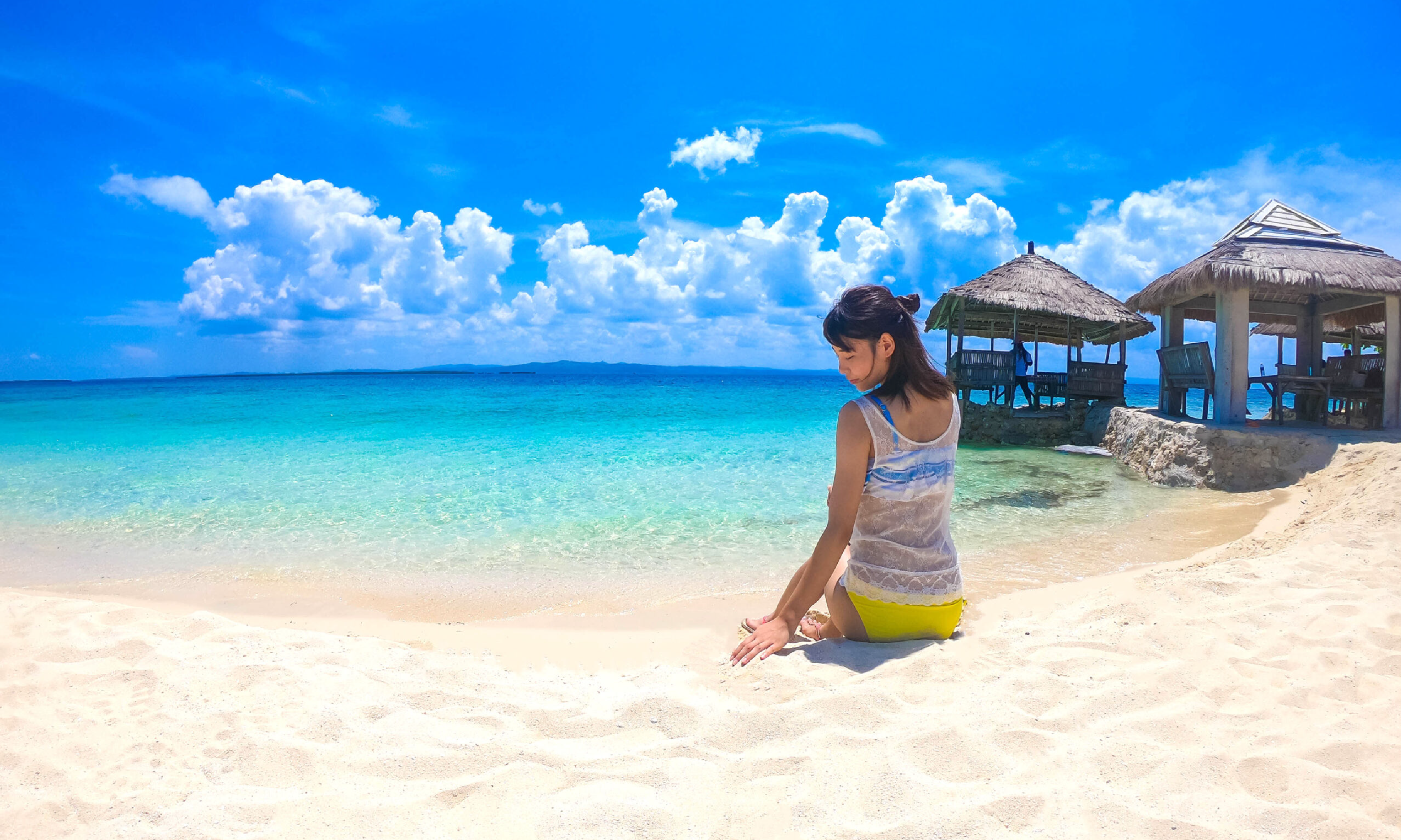 白い砂浜、真っ青なビーチをバックに写真を撮る一人の女性
