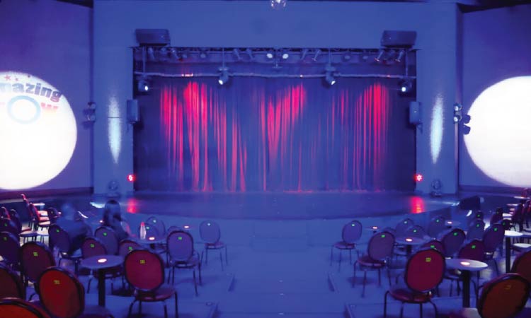 始まる前の会場内の様子
会場全体は薄暗く、両サイドに丸い机と椅子がセットになって置かれている
正面にはステージがあり、赤いカーテンが閉めれれている